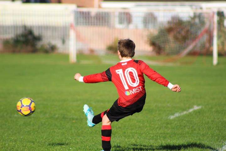 little boy kicking a football with a iMist sponsored shirt on